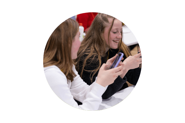 Circular image of two people looking at their phones and smiling.