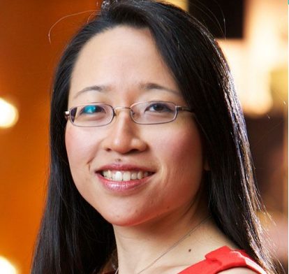 Dr Eugenia Cheng wearing a red dress smiling in front of a warm toned background.