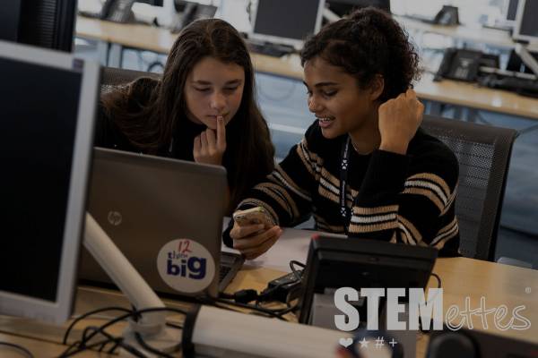Two Stemettes sitting in a room of computers and looking at a phone together.