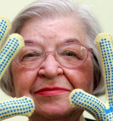 Stephanie Kwolek in Kevlar gloves smiling in front of a yellow background.