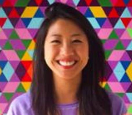 Brina Lee wearing a purple shirt smiling in front of a geometric background.