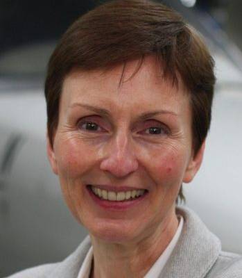 Helen Sharman wearing a grey blazer smiling in front of a grey background.