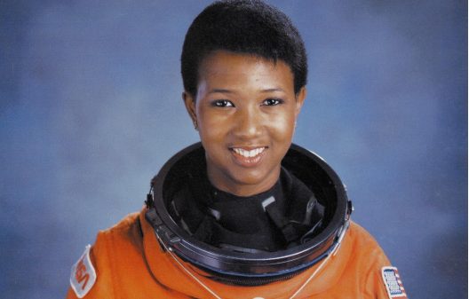 Dr Mae Jemison wearing an astronaut suit and posing in front of a blue background.