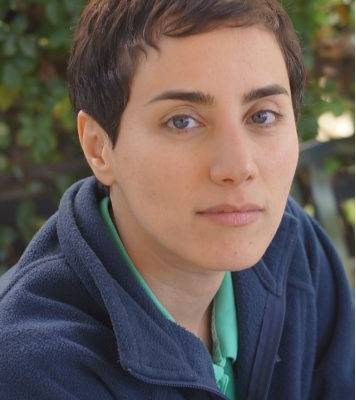 Maryam Mirzakhani wearing a blue fleece posing in front of a leaf - filled background.