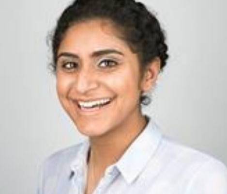 Pooja Godhania wearing a spotty shirt smiling in front of a white background.