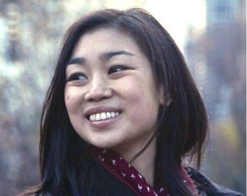 Tracy Chou wearing a dark red scarf smiling in front of a city scape.