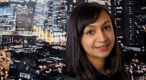 Roma Agrawal smiling in front of a wall decorated with the London at night.