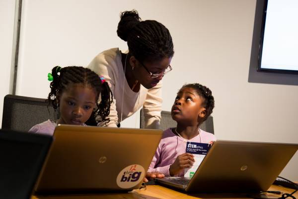 Two young Stemettes and an older Stemette working together on laptops.