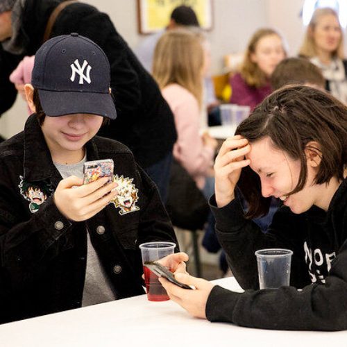 Two people laughing together at their phones at a Stemettes event.