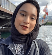 Aisha Islam wearing a leather jacket smiling against an urban background with a river.