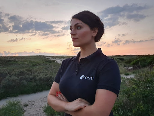 Nicol Caplin wearing an ESA shirt posing in front of a setting sun landscape.