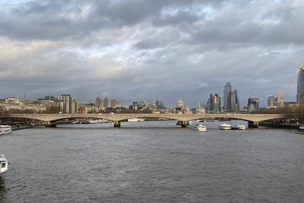 Waterloo bridge from a side view, with water and building seen in the foreground and background. Boats can be seen in the water at the bottom.