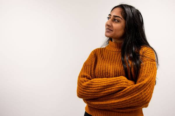 Stemettes Hero Ayushi poses in front of a white background. She is wearing an orange jumper.