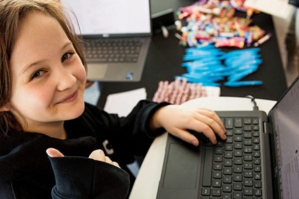 A junior Stemette on a laptop, holding their thumb up to the camera.