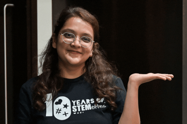 GIF of TeamStemette Himani smiling and posing against a dark wall
