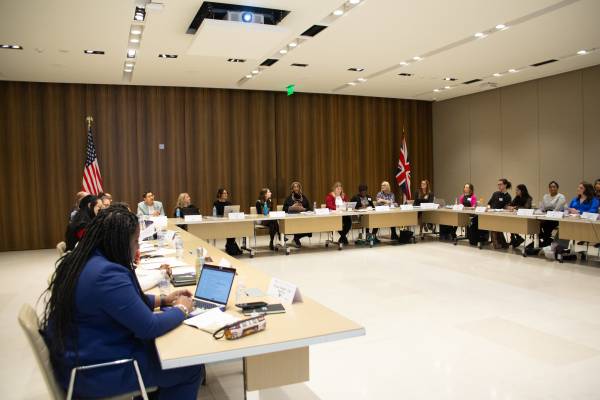 A U-shaped table in the middle of a room with approximately 20 people sitting around it. The room is at the US Embassy.