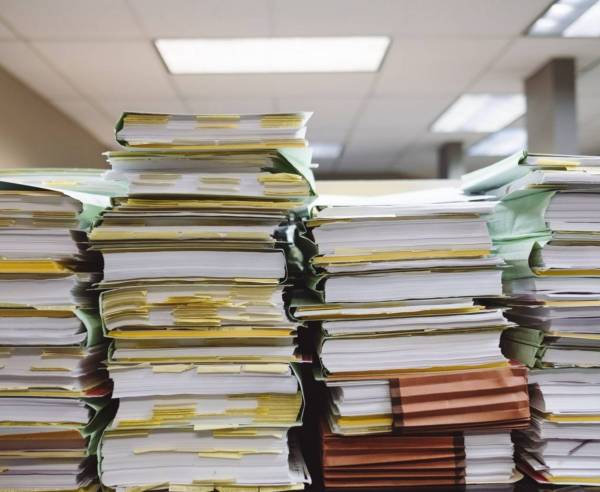 4 stacks of files and papers of varying heights in an office.