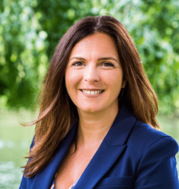 Jane Ashworth smiles at the camera in front of a green background. She is wearing a blue blazer.