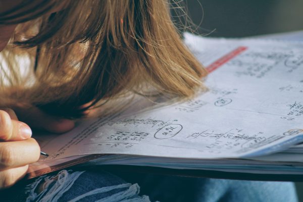 A young person writing on a piece of paper. They have blonde hair.
